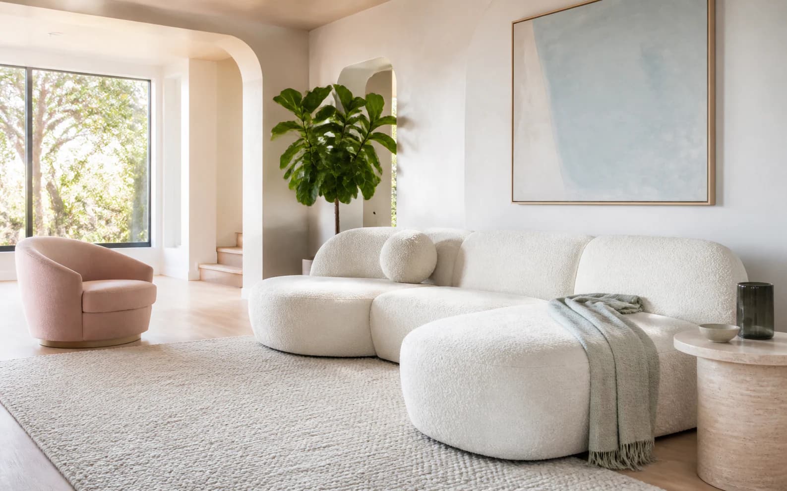 Bright living room with a cream boucle sectional, pale rug, curved architecture, and powder-blue art